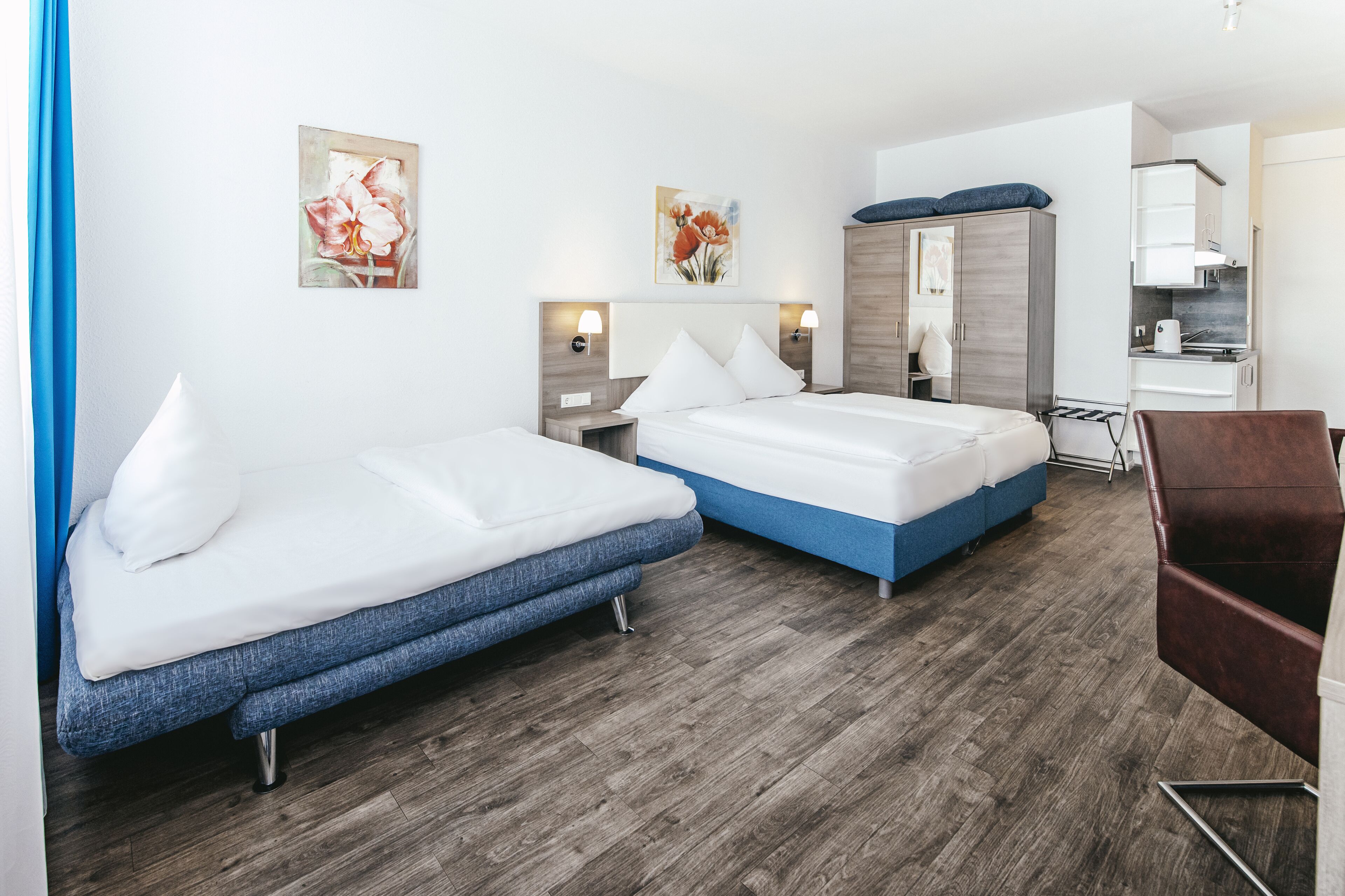 Ein Hotelzimmer mit zwei Betten, Holzboden, Schrank, Schreibtisch und Stuhl.
