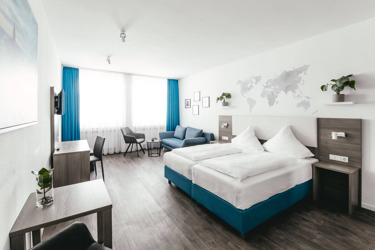 A modern hotel room with a large bed, a desk, a chair, and a small table.