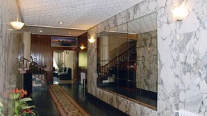 A hotel lobby with marble walls, a grand staircase, and a large mirror reflecting the interior. - Hotel América (Ferrol)