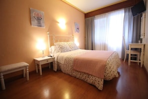 Un dormitorio con cama, mesitas de noche, un banco, un escritorio y televisión.