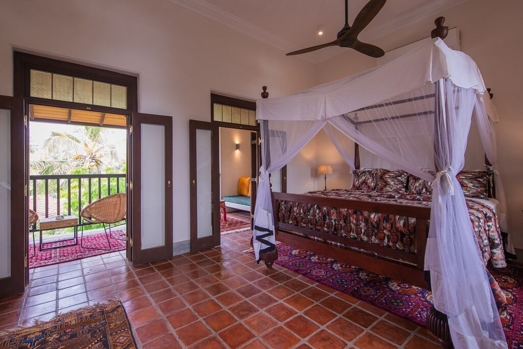 Un dormitorio con una cama bajo un dosel, un balcón con sillas y vistas a la vegetación.