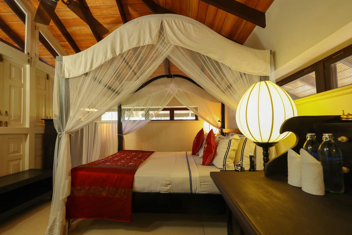 A bedroom with a canopy bed, a bedside table with bottles, and a lamp.