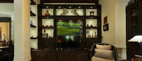 A living room with a flat-screen TV, wooden shelves, and a comfortable chair.