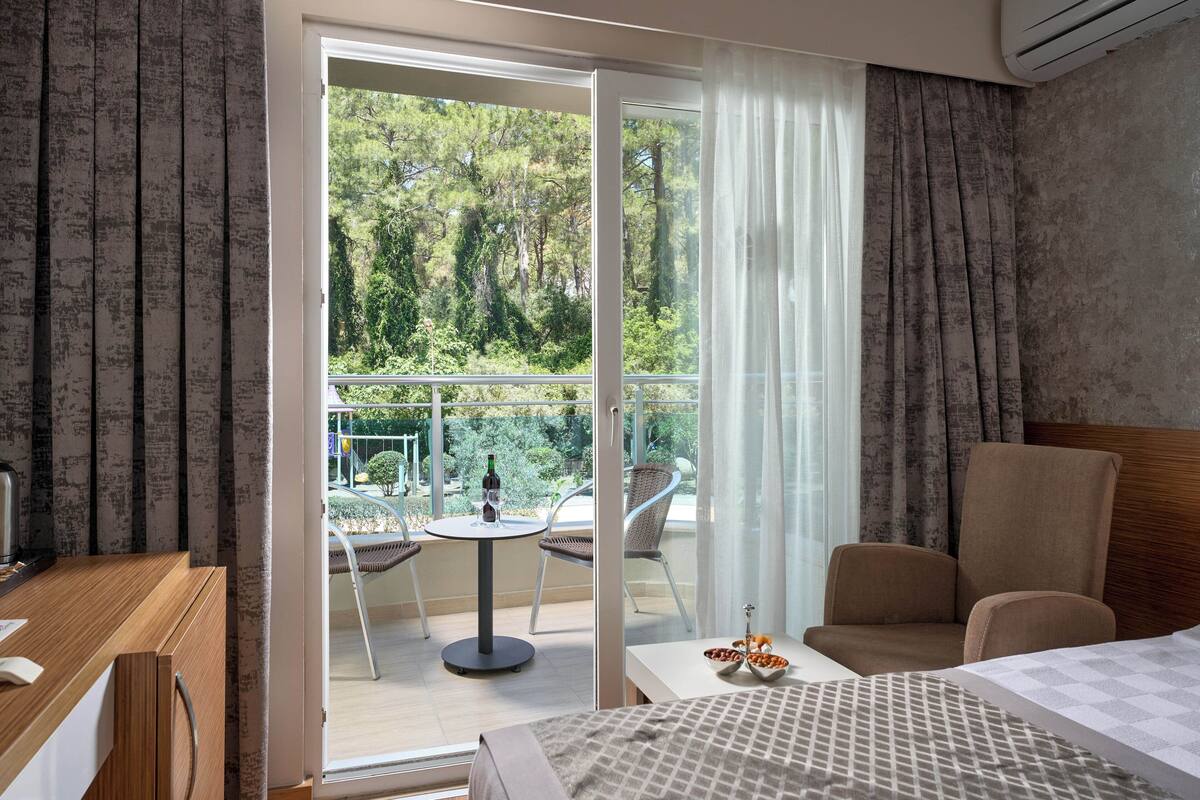 Hotelkamer met een bed, bureau, stoel, klein tafeltje met een fles en een kom, en een balkon met een tafel en stoelen.