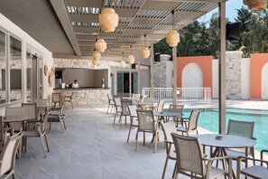 Un patio exterior con mesas y sillas, una piscina y un muro de piedra.