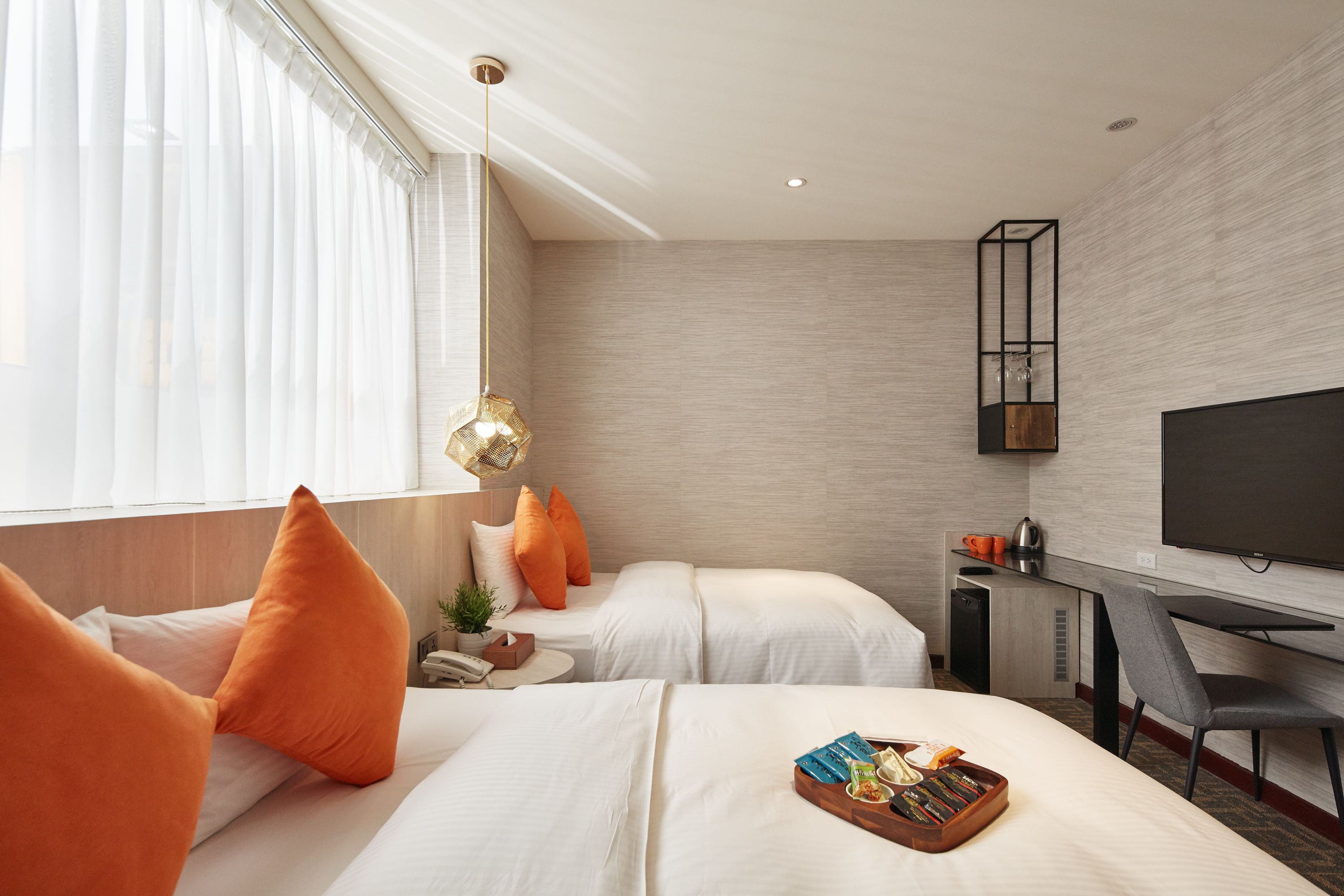 Een hotelkamer met twee bedden, een bureau, een televisie en een raam met gordijnen.