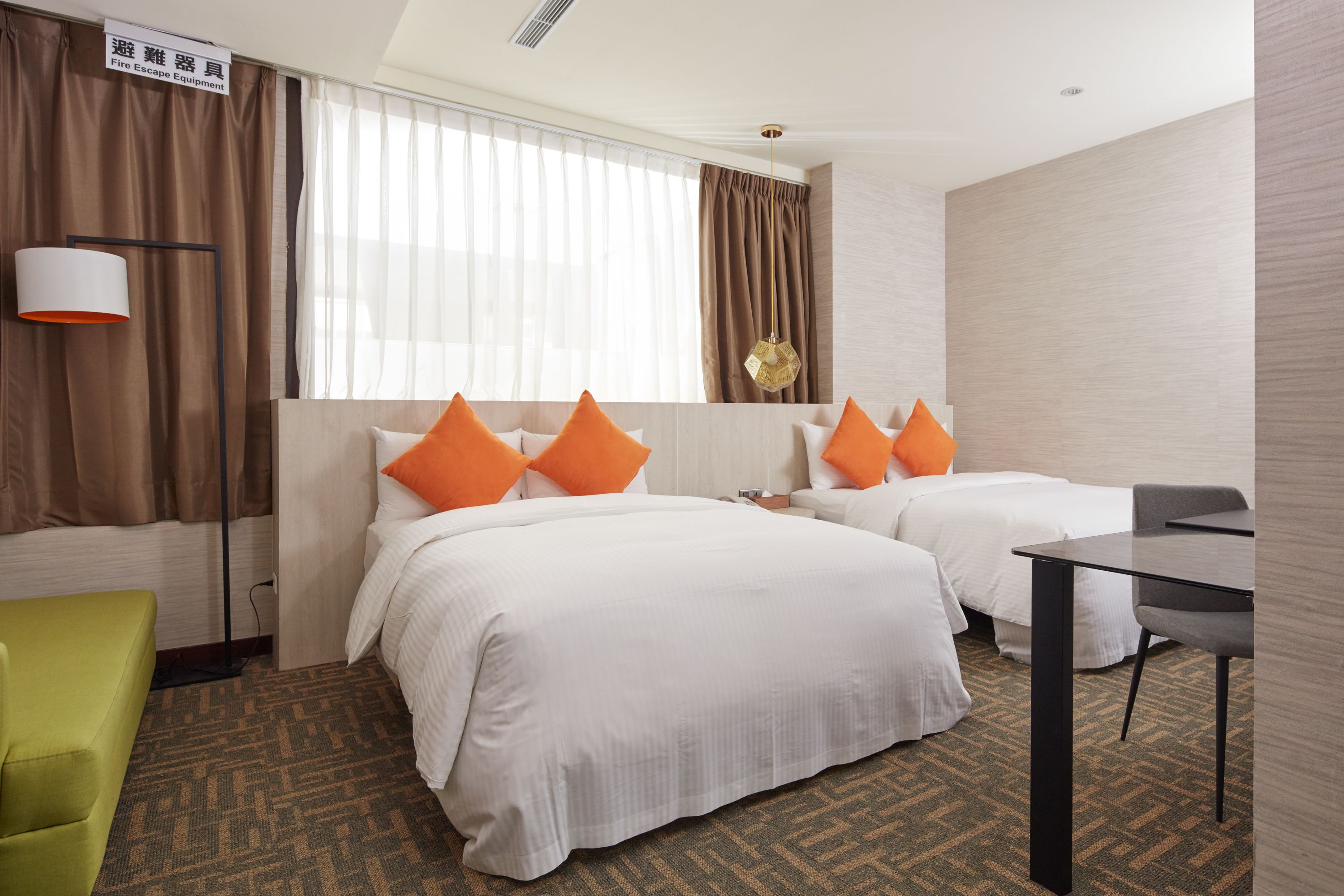 A hotel room with two beds, a desk, a chair, and a lamp.