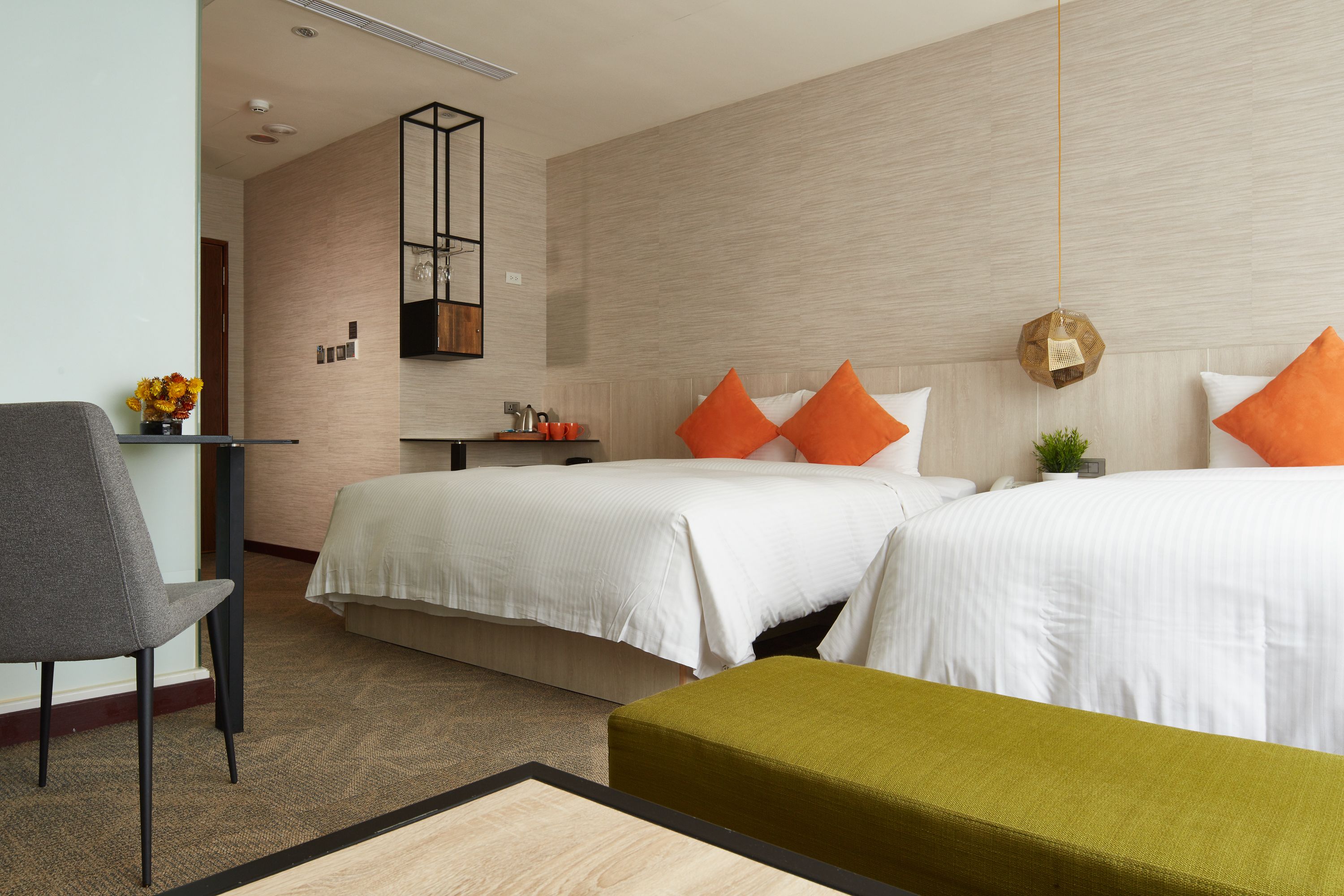 A hotel room with two beds, a desk, a chair, and a small table with a vase of flowers.