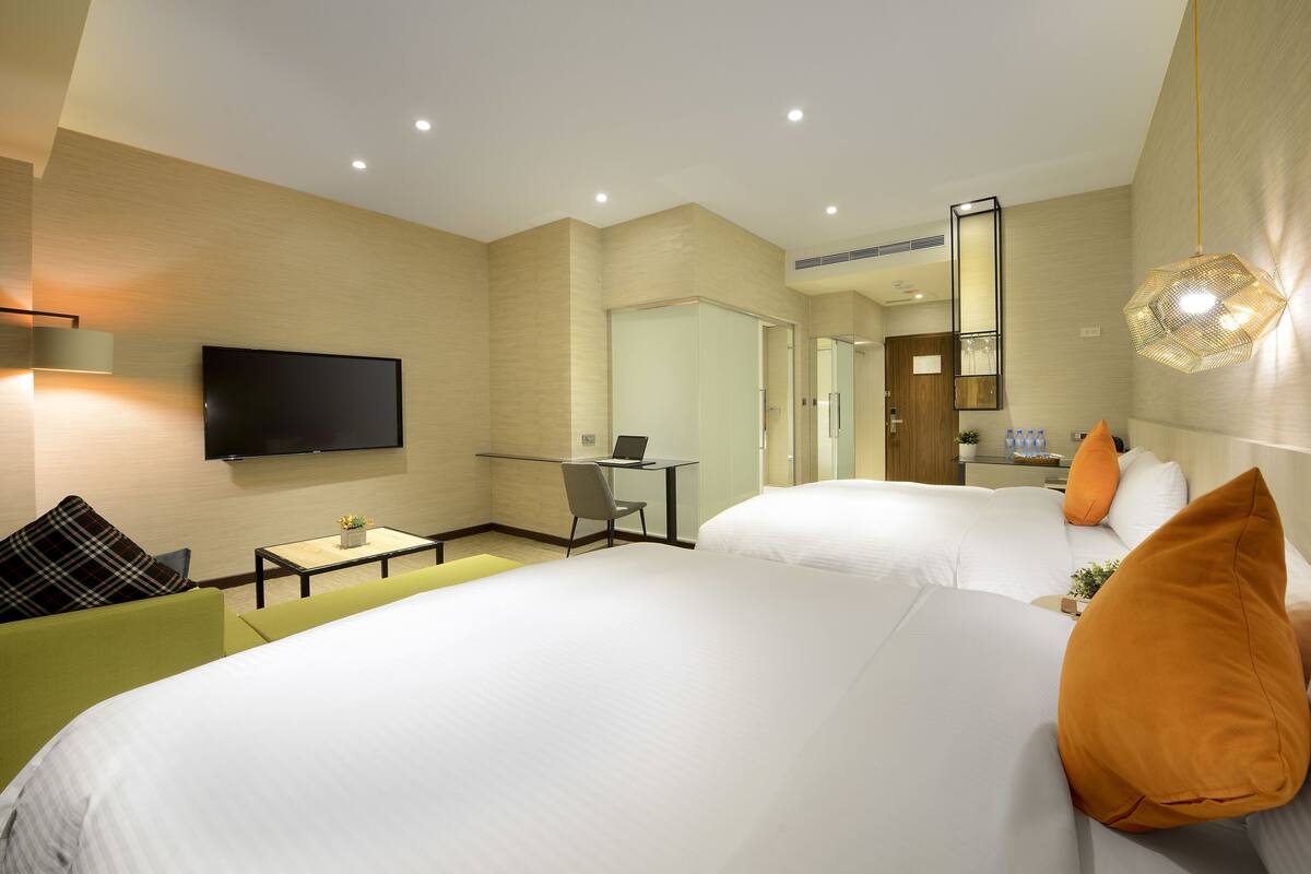 A hotel room with two beds, a desk, a chair, a TV, and a mirror.