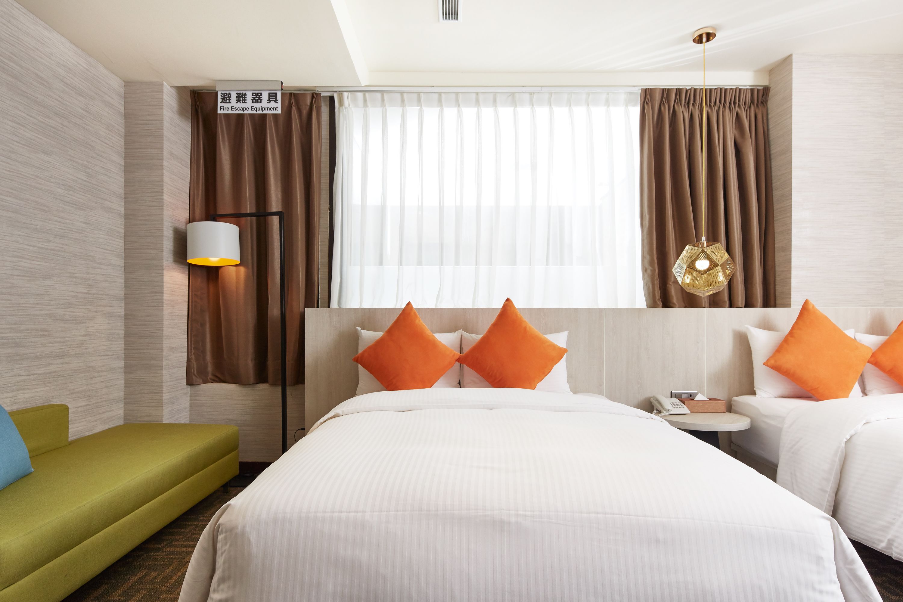 Une chambre d’hôtel comprenant un lit, deux oreillers, une table de chevet, une lampe, une chaise et un panneau indiquant l’emplacement du matériel de sécurité incendie.