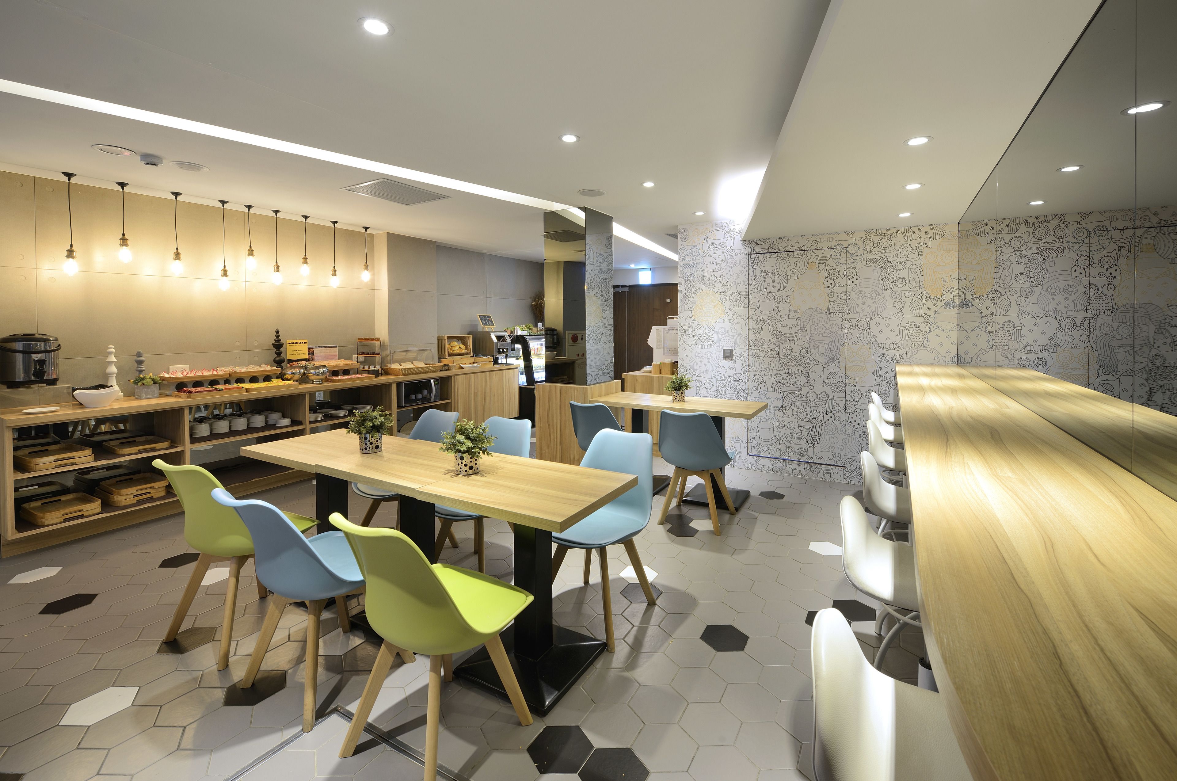 A modern restaurant with wooden tables and chairs, a kitchen area, and a patterned wall.