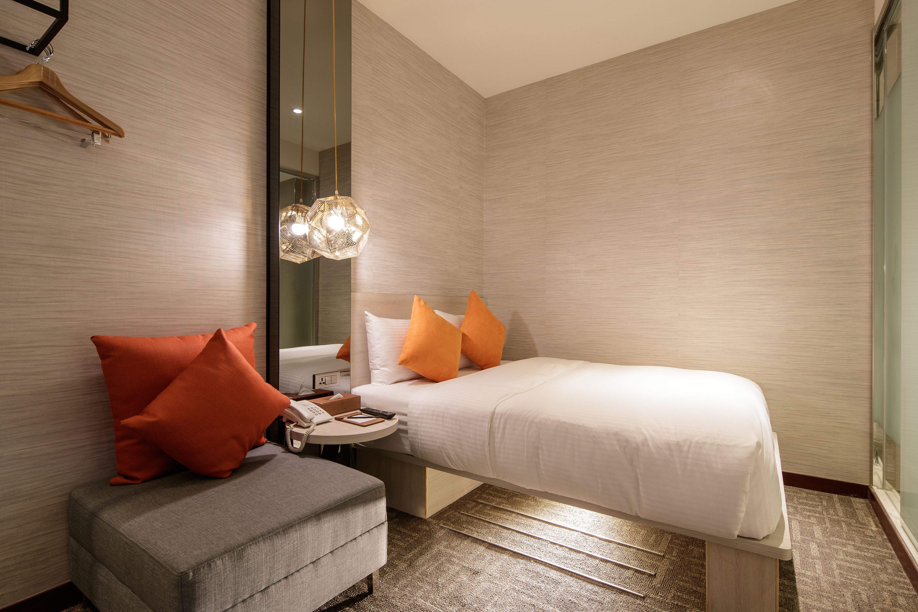 A modern hotel room with a bed, a bedside table, a chair, and a large mirror.