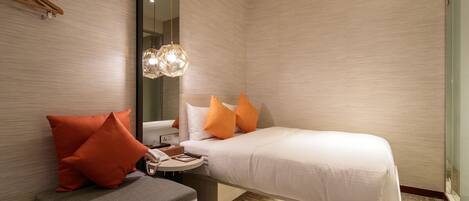 A modern hotel room with a bed, a bedside table, a chair, and a large mirror.