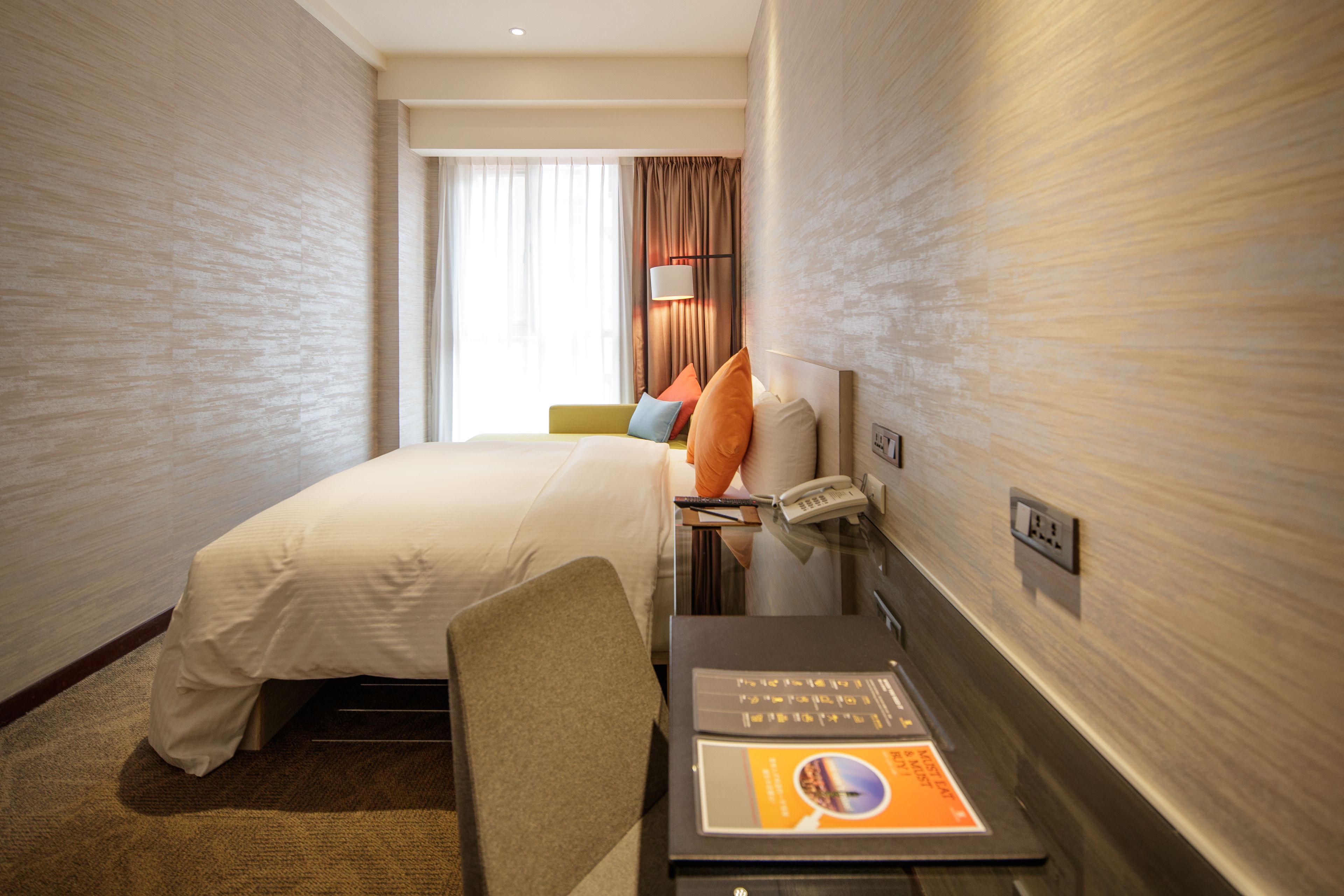 A hotel room with a bed, a desk with a phone, and a lamp.