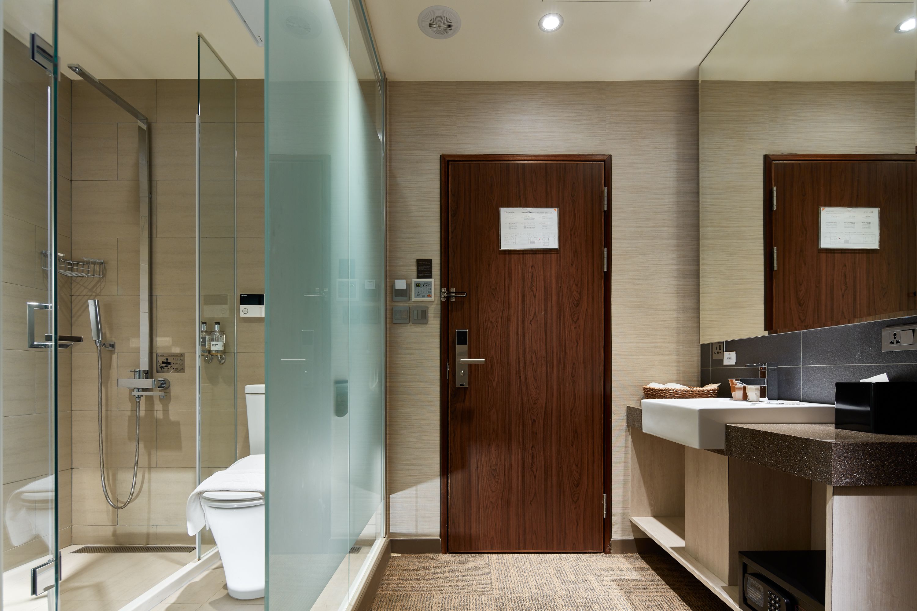 A modern bathroom with a glass-enclosed shower, a wooden door, and a sink with a mirror.