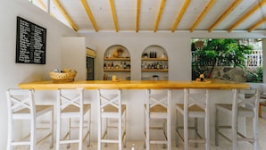 A bar area with a wooden counter, white bar stools, and shelves with bottles. - Golden Lighthouse Hotel (Kas)