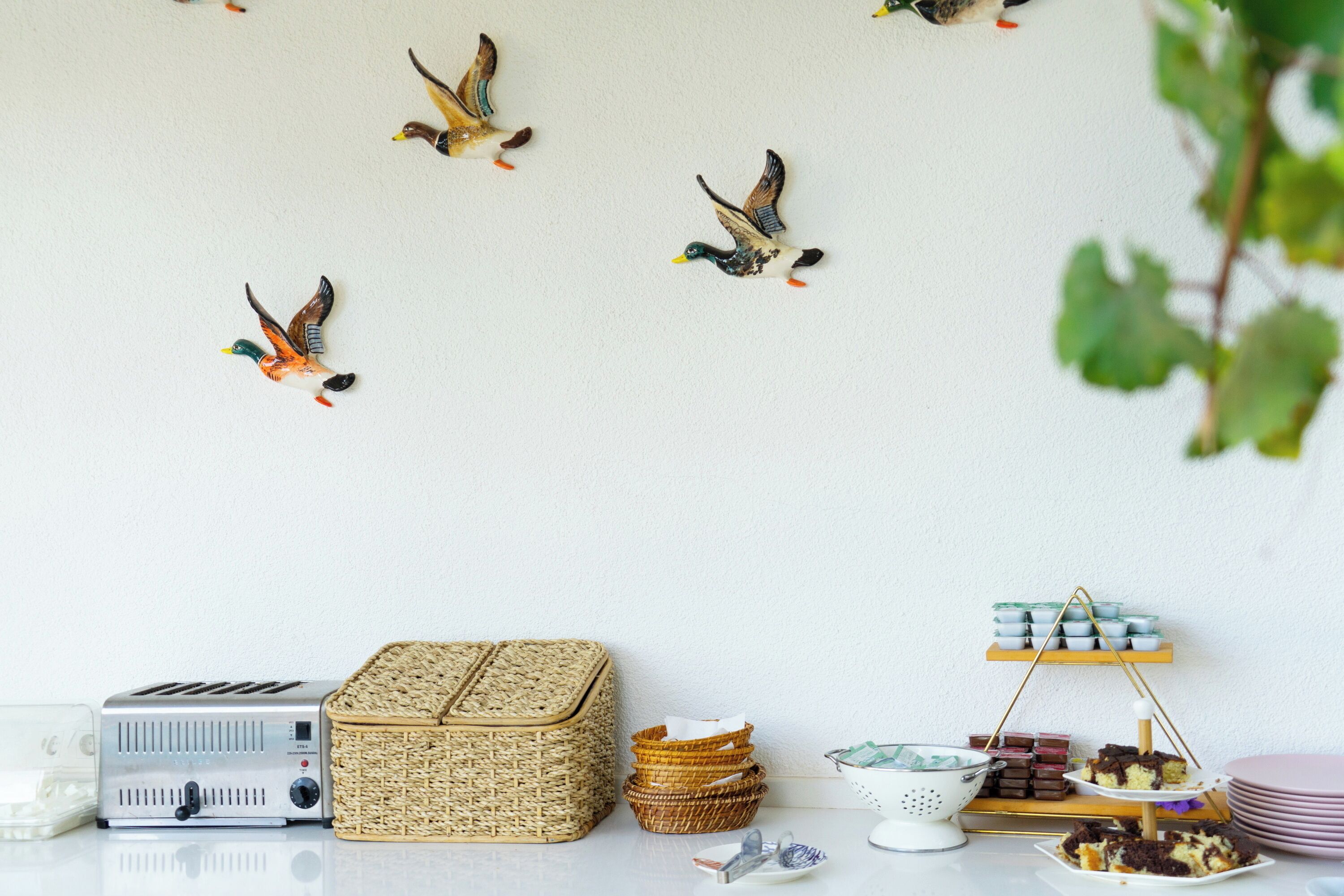 A table with a toaster, wicker baskets, a stack of plates, and a dessert display.