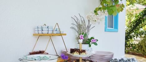 A table with a variety of food items, including brownies and a bowl of cookies, set against a white wall with a blue window frame.