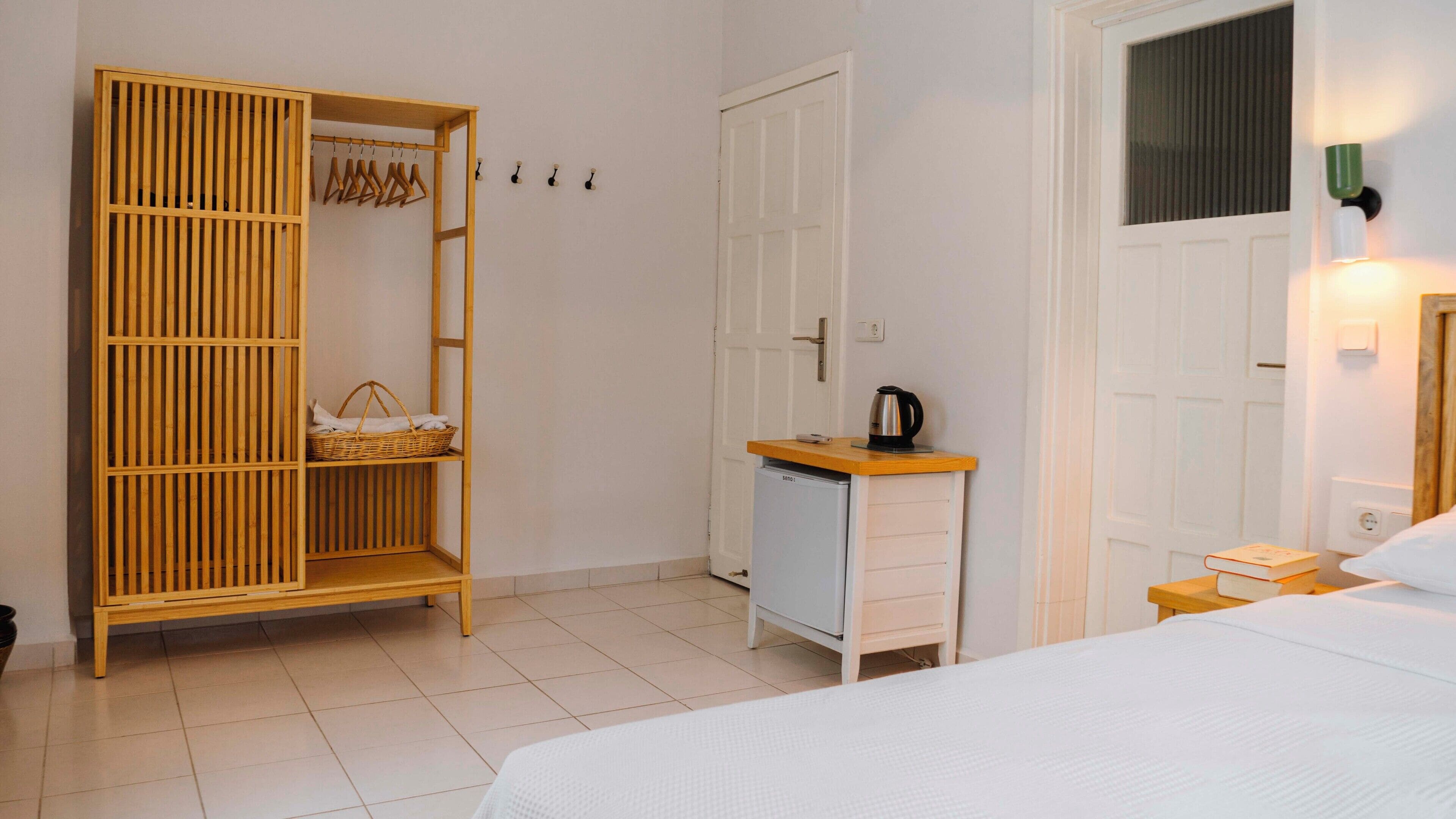 Une chambre à coucher avec un lit, une armoire où sont suspendus des vêtements, une petite kitchenette et une table de chevet avec un livre.