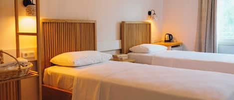 Une chambre d’hôtel avec deux lits, une table de chevet avec une bouilloire, une lampe et une fenêtre avec des rideaux.