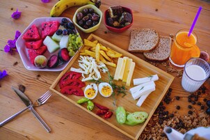 Una mesa de madera con diversos alimentos, como frutas, queso, pan y un vaso de jugo de naranja.