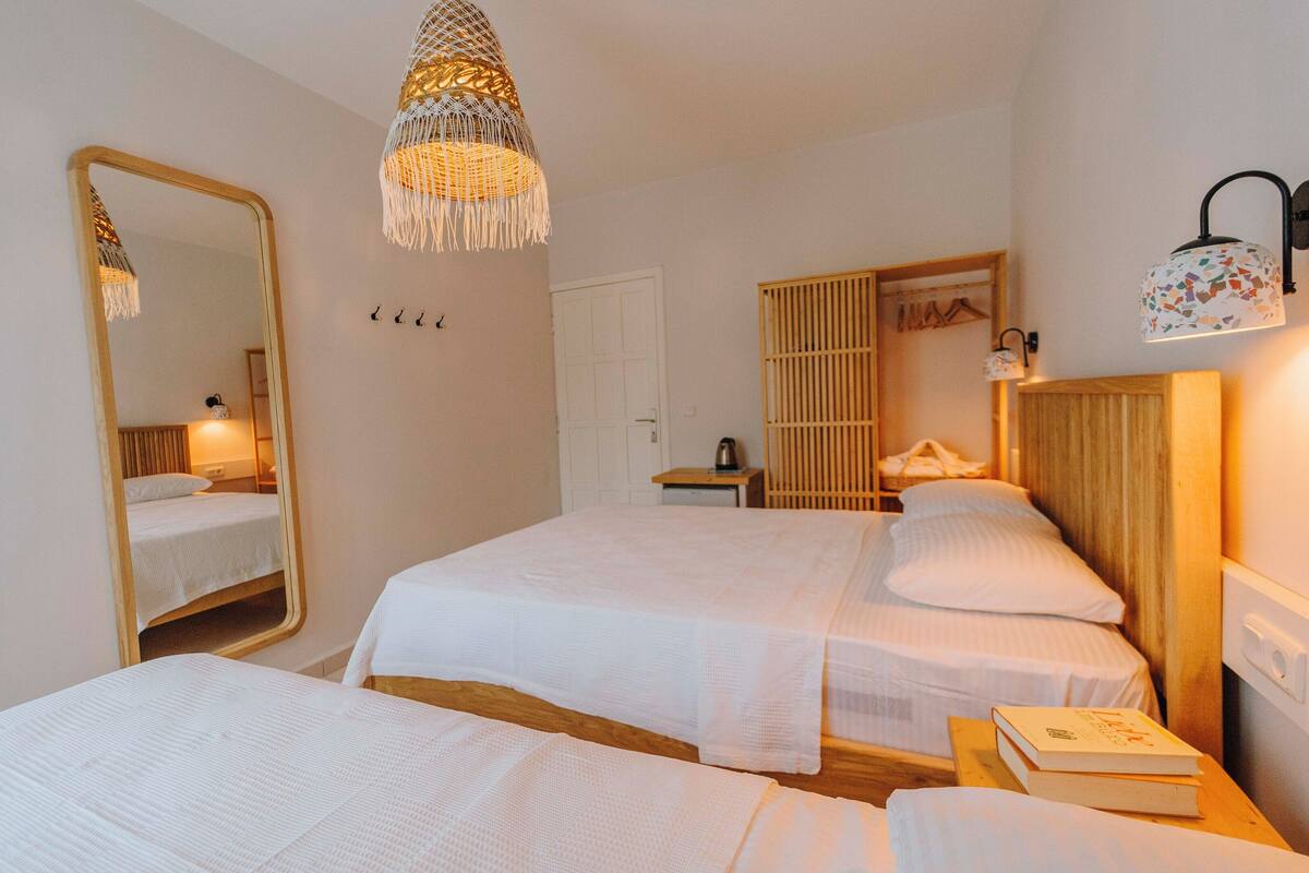 A hotel room with two beds, a large mirror, a hanging light fixture, a wardrobe, and a bedside table with a book.