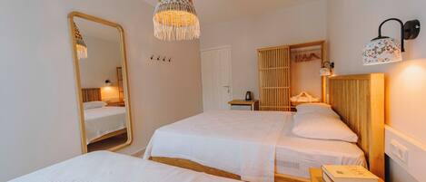 A hotel room with two beds, a large mirror, a hanging light fixture, a wardrobe, and a bedside table with a book.