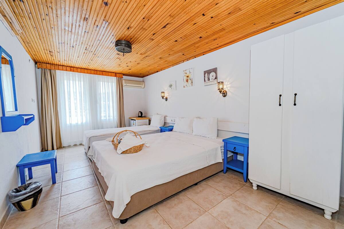 A bedroom with a wooden ceiling, white walls, a large bed, a wardrobe, a nightstand, and a small table.