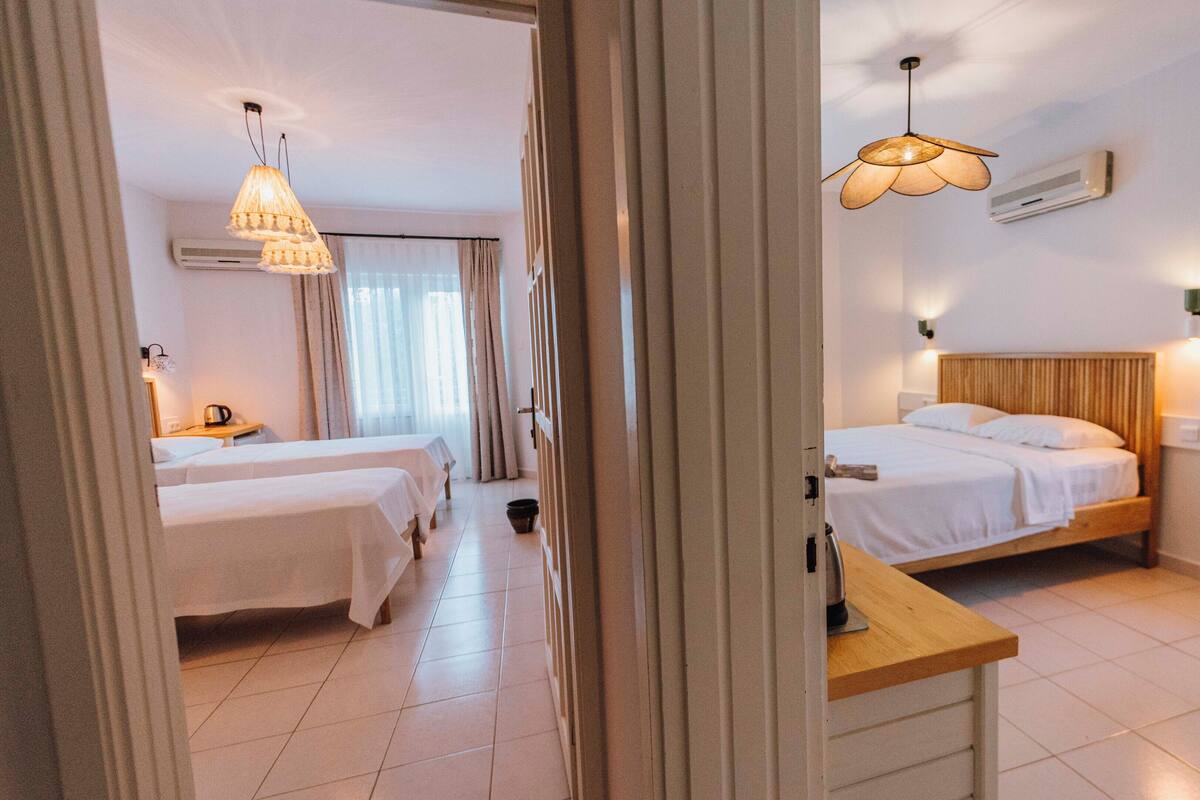 A hotel room with two beds, a wooden nightstand, a ceiling fan, and a window with blinds.