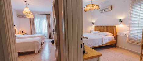 Habitación de hotel con dos camas, una mesita de noche de madera, un ventilador de techo y una ventana con persianas.
