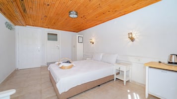 A bedroom with a wooden ceiling, a bed, a bedside table, a desk, and a refrigerator.