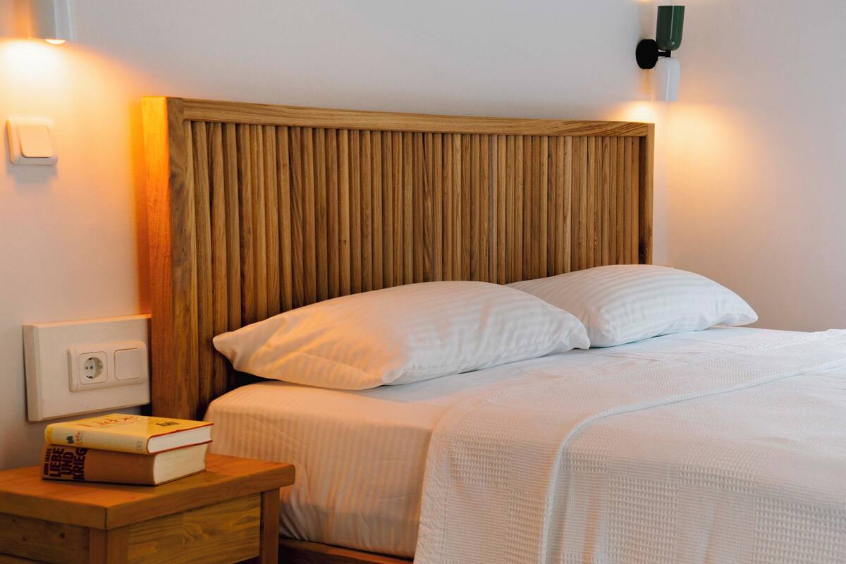 A neatly made bed with white linens, a wooden headboard, and a bedside table with a book and a lamp.