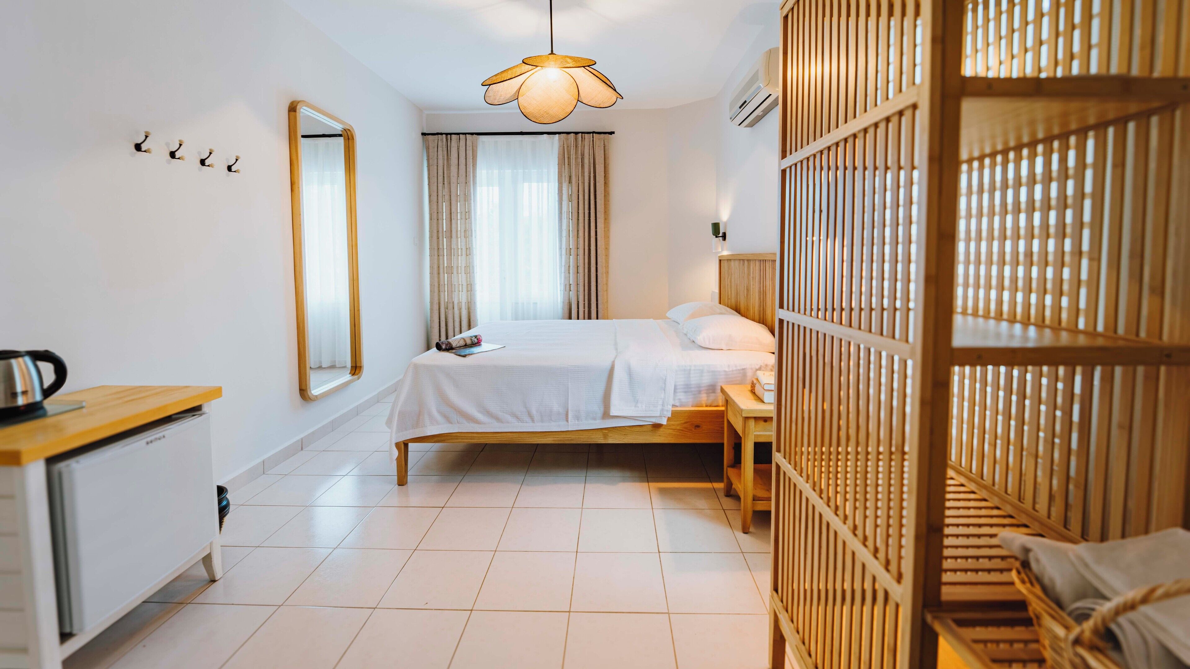 Habitación de hotel con cama, escritorio, espejo, lámpara colgante y un separador de madera.