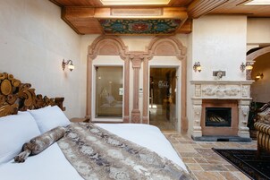 A bedroom with a large bed, a fireplace, and a view of the hotel lobby.