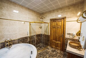 A bathroom with a bathtub, a shower enclosure, a wooden door, and a sink with a gold faucet.