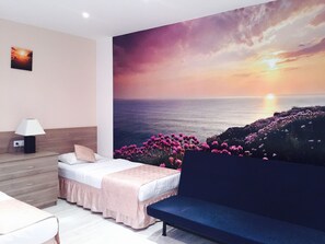 Relax in a serene space with a stunning ocean sunset mural, a comfortable bed, and a cozy sofa.