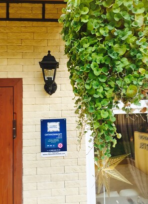 City Comfort Hotel features a charming entrance with a brick wall, wooden door, and a hanging plant.