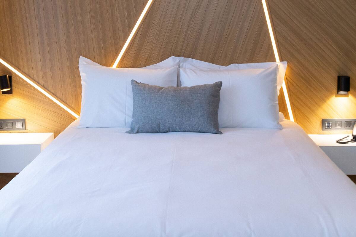 Una habitación de hotel moderna con una cama grande, pared de paneles de madera y lámparas geométricas.