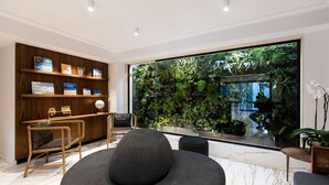 Un interior moderno con un ventanal amplio, una estantería, una zona de estar y un pequeño jardín interior.