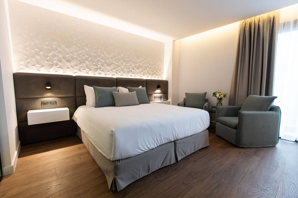 Una habitación de hotel moderna con una cama grande, una mesita de noche, una silla y un panel decorativo en la pared.