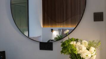 A round mirror on a wall, a vase with white flowers, and a white countertop.