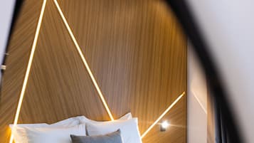Una habitación de hotel moderna con cabecera de madera, ropa de cama blanca y una mesita de noche con lámpara.