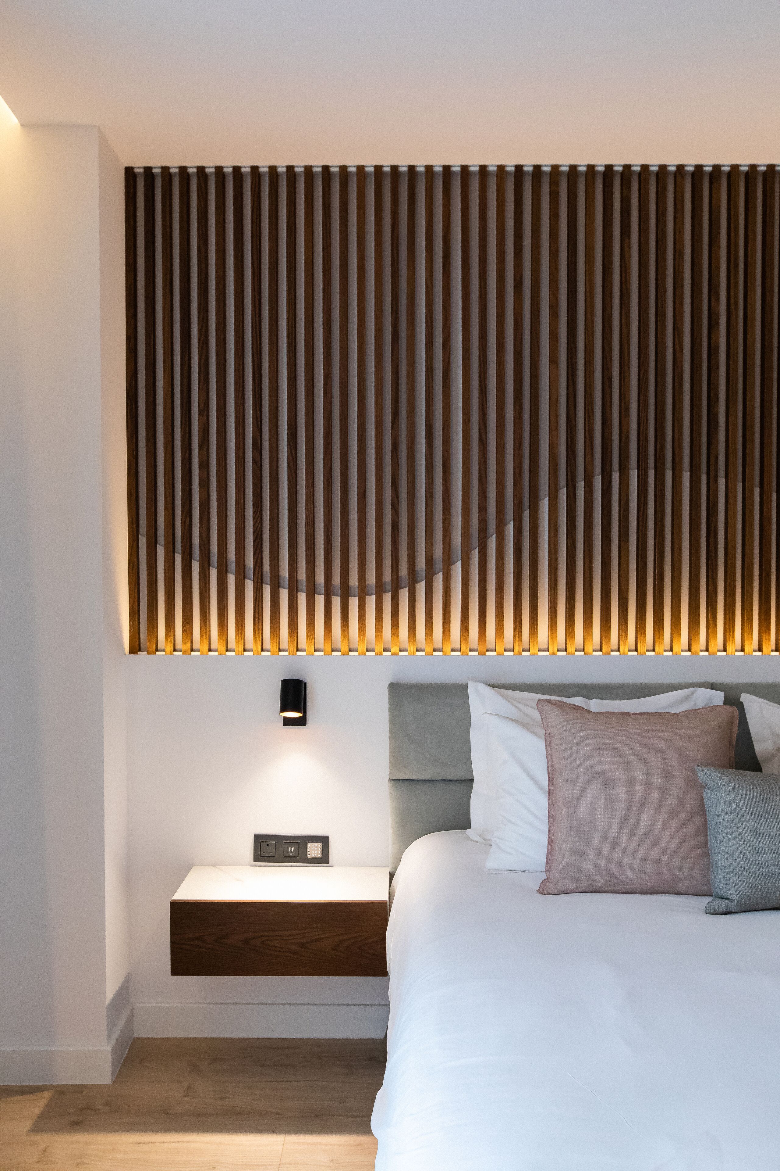 A modern bedroom with a bed, bedside table, and a wall-mounted light fixture.