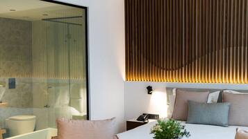 A modern hotel room with a large bed, two armchairs, a small table with a vase, and a large mirror.