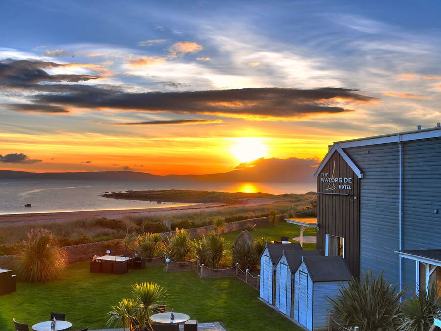 A hotel with a view of the sunset over the sea, a grassy lawn, and outdoor seating.