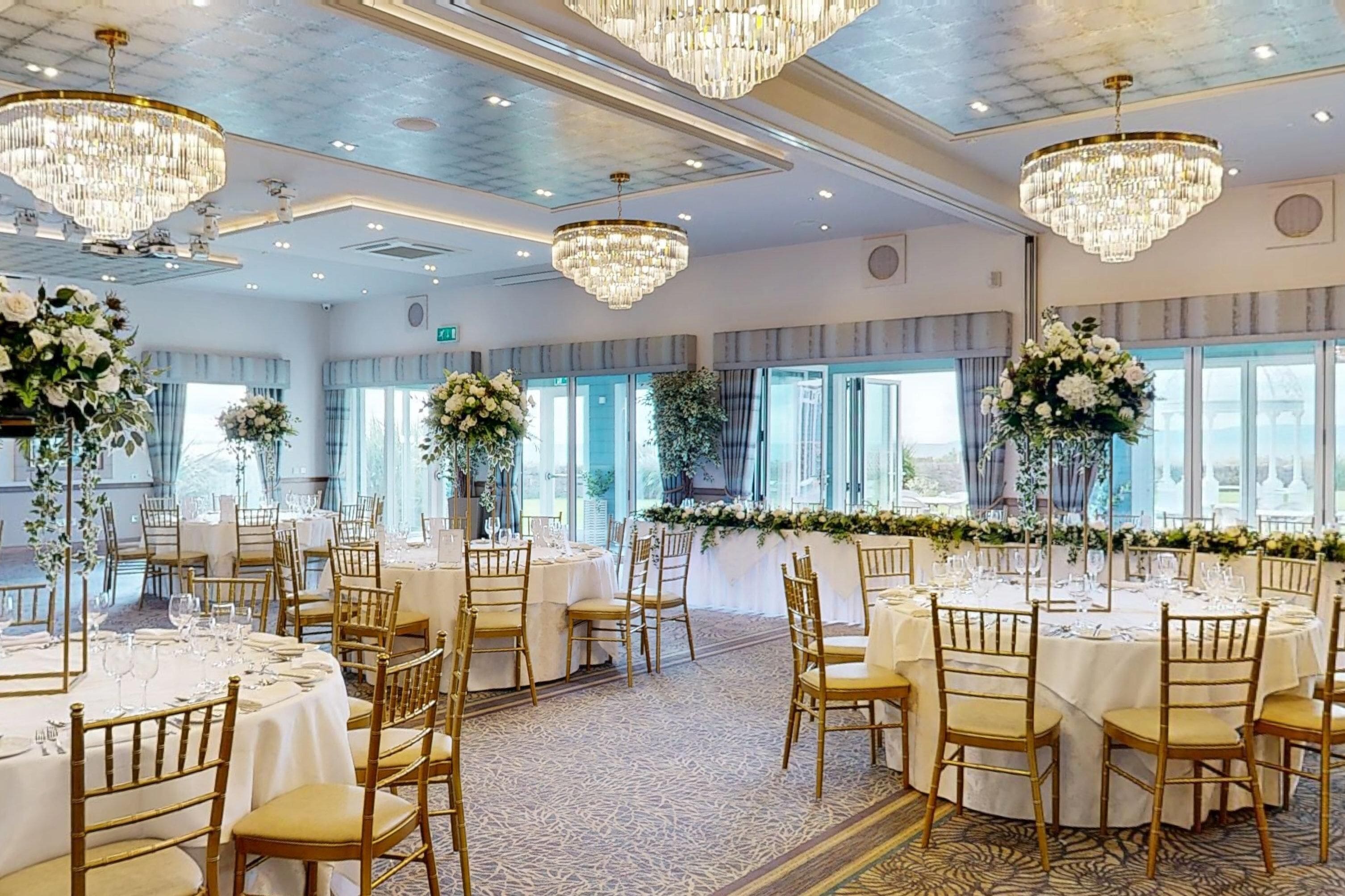 Un salón de banquetes con mesas redondas, sillas doradas y candelabros.
