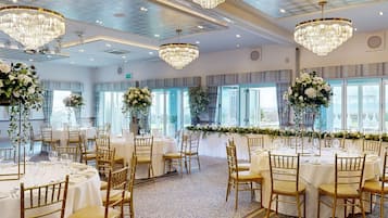 Un salón de banquetes con mesas redondas, sillas doradas y candelabros.