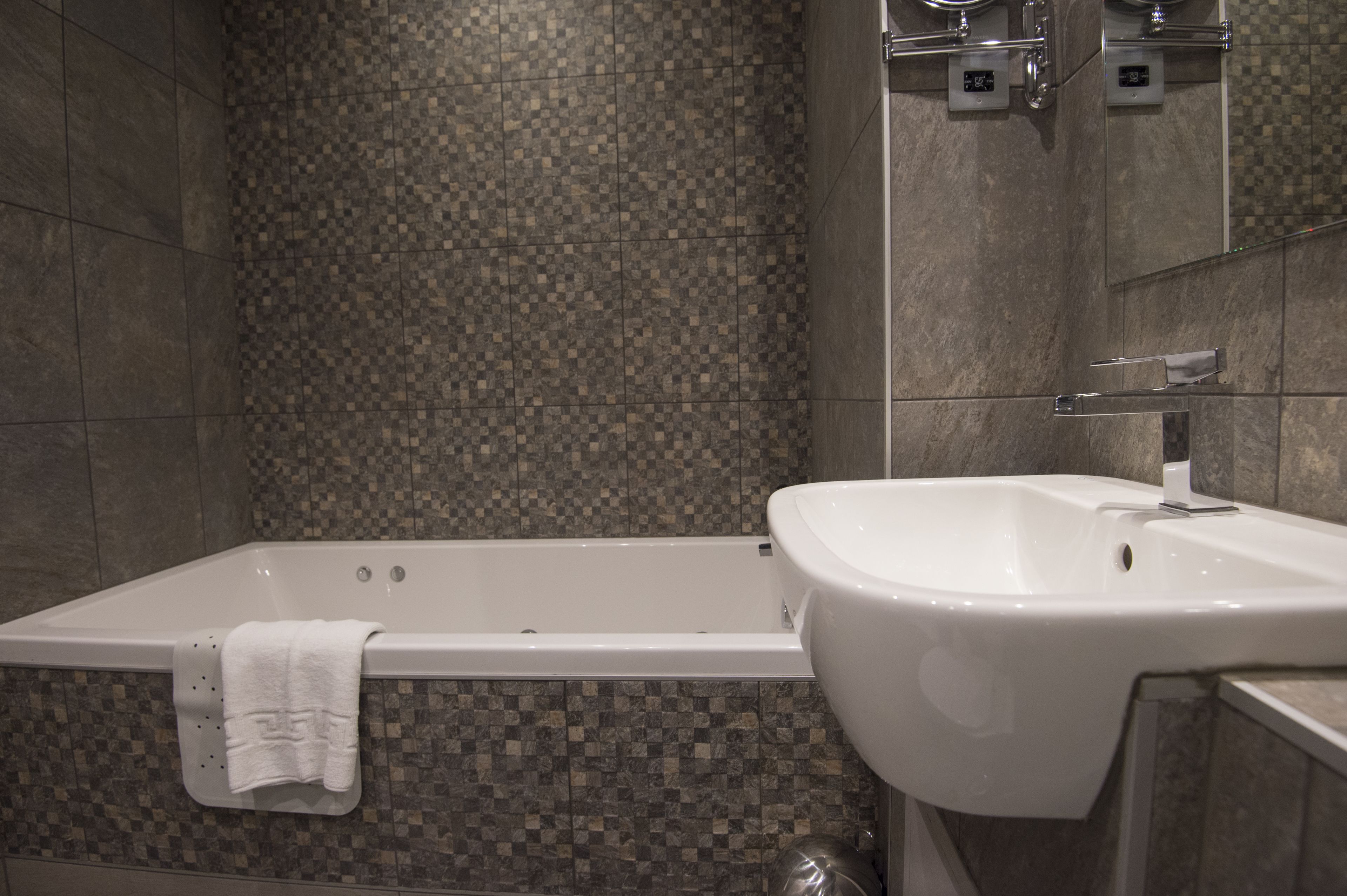 A modern bathroom with a checkered tile wall, a white bathtub, and a white sink.