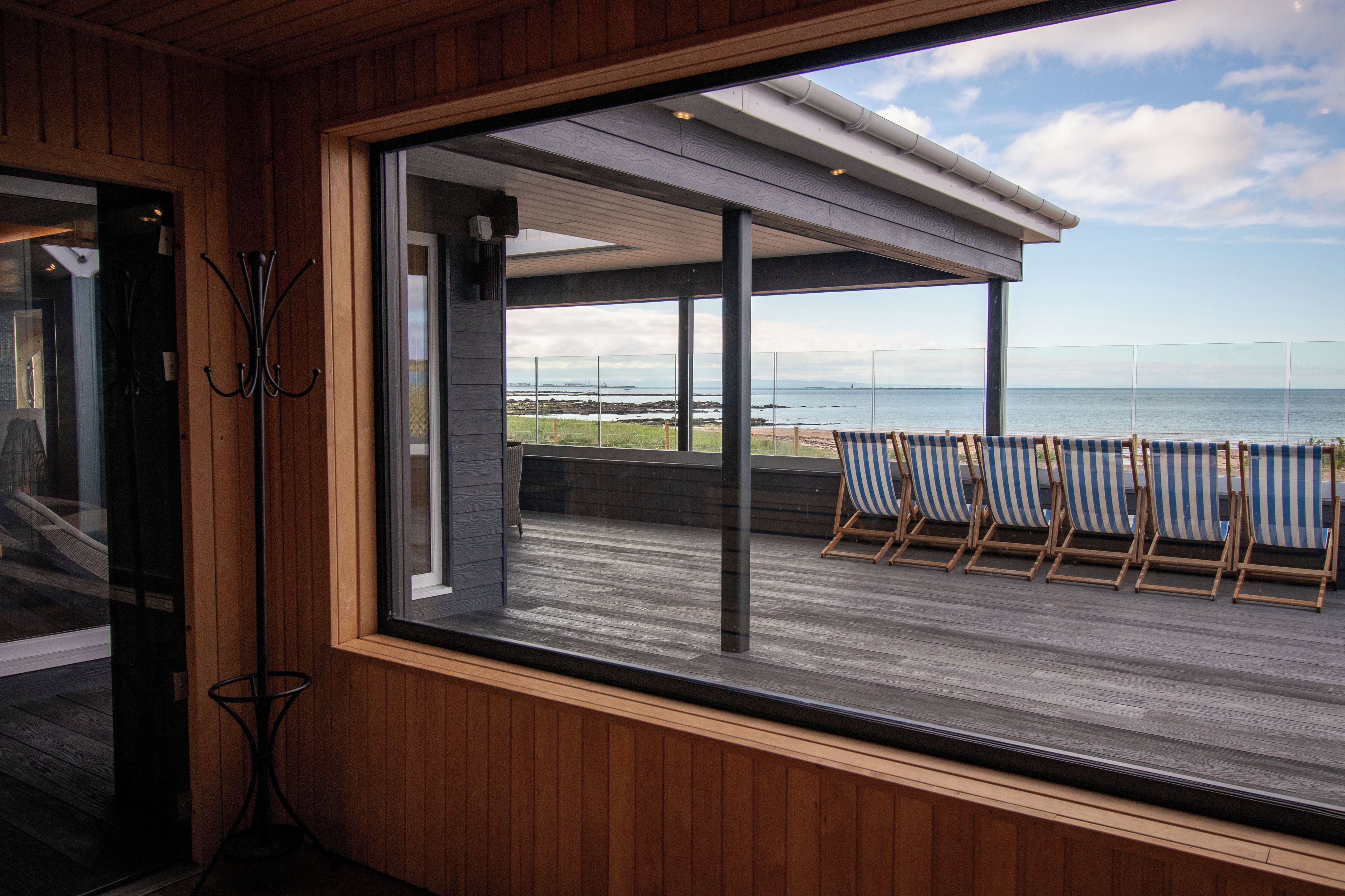 A room with a large window overlooking a beach with lounge chairs.