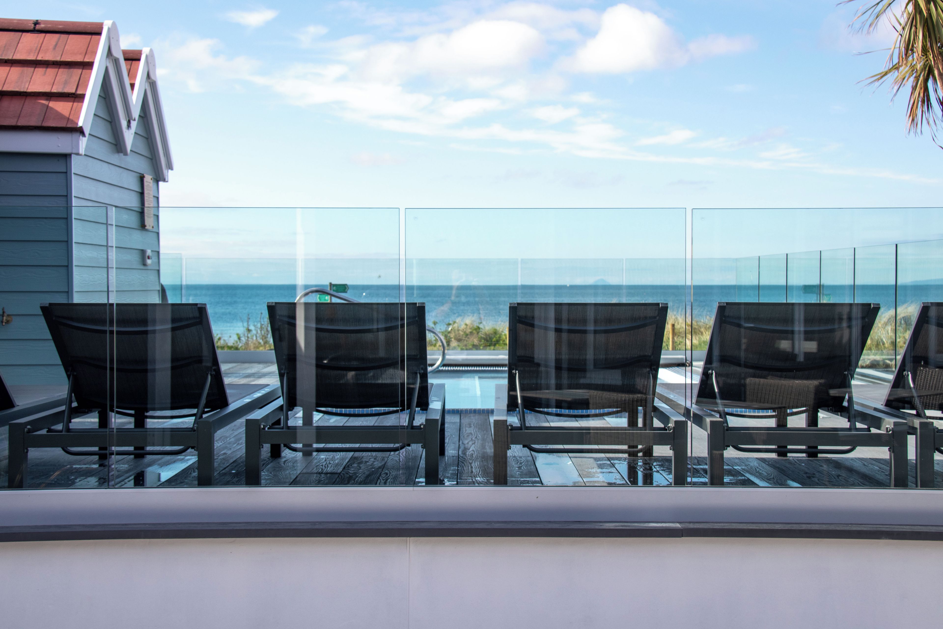 A balcony with four chairs facing a pool and the ocean.